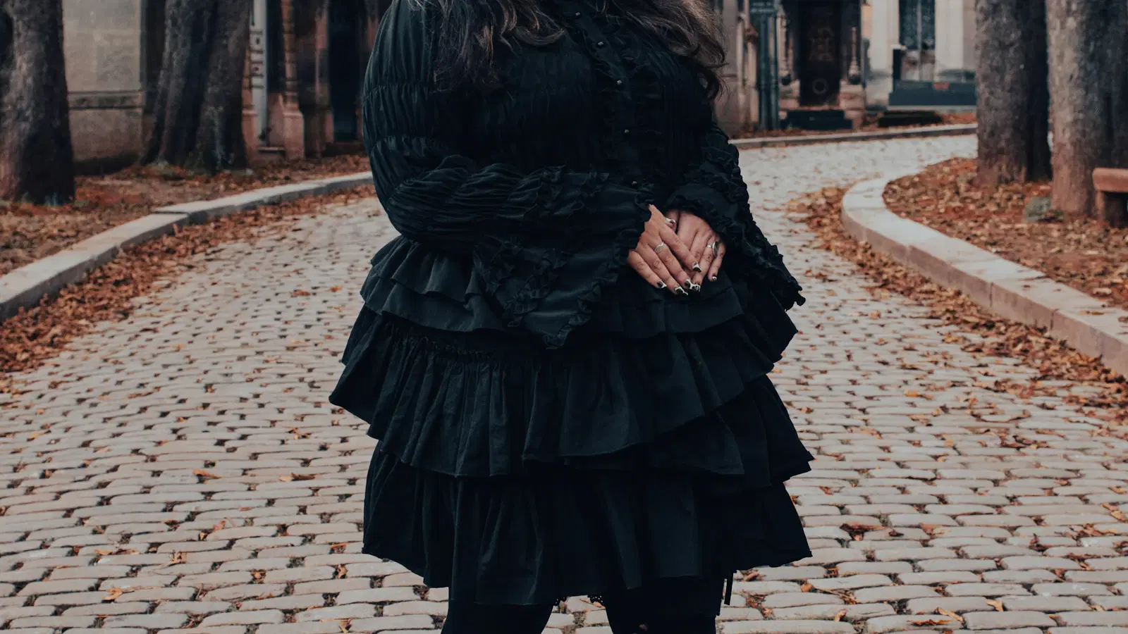 Gothic femboy makeup products laid out — BB cream, black eyeliner, smoked grey eyeshadow, matte berry lip, and a fine brow brush