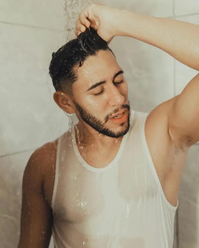 A person applying leave-in conditioner to beard and chest hair in a shower